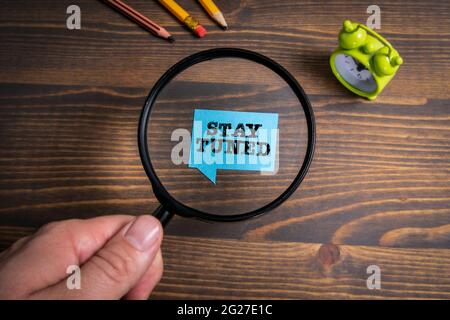 Bleib Dran. Sprechblase und grüner Wecker auf einem hölzernen Hintergrund. Stockfoto