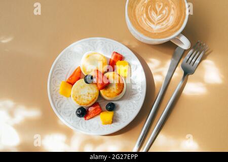 Hüttenkäse-Pfannkuchen auf dem Teller, Tasse Kaffee. Syrniki mit Beere, Draufsicht. Stockfoto