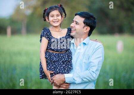 Happy Young indian weiter mit seiner niedlichen kleinen Tochter, die auf grünem Ackerfeld Hintergrund, Familie Bindung. Stockfoto