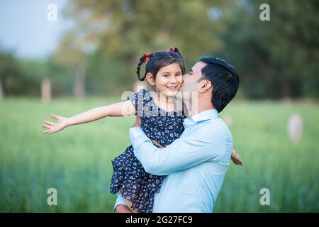 Happy Young indian weiter küssen seine niedliche kleine Tochter stehen bei grünen Landwirtschaft Feld Hintergrund, verspielt, Familie Bindung. Stockfoto