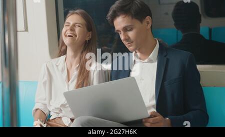 Junge kaukasische weiße Geschäftsfrau und Mann, die mit einem Laptop sitzen Computer arbeitet zusammen im Gespräch auf der U-Bahn-Zug in der Morgen während des Ausgehend zu Stockfoto