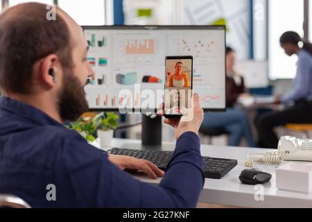 Behinderter, ungültiger Manager, der während der Arbeitszeit mit Freunden, die das Smartphone halten, auf Videocall spricht. Im Rollstuhl sitzender Mitarbeiter, der im Finanzbüro arbeitet. Stockfoto