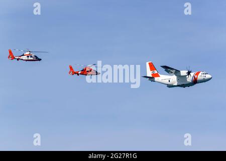 Eine US-Küstenwache C-27J, die in Formation mit zwei MH-65 Dolphin-Hubschraubern fliegt. Stockfoto