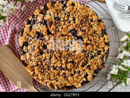 Traditional german cherry crumble cake on a cooling rack on rustic and wooden table background with cherry blossoms Stockfoto