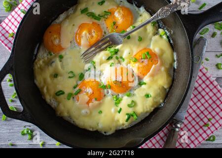 Spiegeleier mit Käse in einer gusseisernen Pfanne. Nahaufnahme und Draufsicht Stockfoto