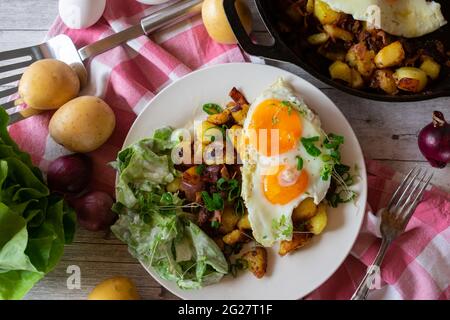 Herzhaftes vegetarisches Landgericht mit Bratkartoffeln, Eiern und Salat mit Sauerrahm-Dressing, serviert auf einem Teller auf rustikalem Holztisch-Hintergrund Stockfoto