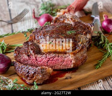 Frisch gegrilltes, trocken gereiftes und irisches Tomahawk-Rib-Eye-Steak auf einem rustikalen und hölzernen Schneidebrett mit Kräutern und Steakmesser Stockfoto