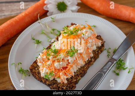 Gesundes vegetarisches Sandwich mit Vollkornbrot, Quark und geriebenen Karotten auf einem Teller mit Messer serviert Stockfoto