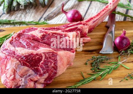 Irisches Tomahawk Rib Eye Steak auf rustikalem Holztischhintergrund mit Messer und Kräutern Stockfoto