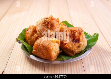 Potato Bonda, ein würziger, indischer Snack, der auf einer Stahlplatte mit Bananenblatt auf traditionelle Weise und isoliert auf einem strukturierten Hintergrund aus Holz serviert wird. Stockfoto