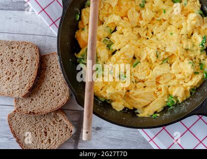 Rührei in einer gusseisernen Pfanne mit Roggenbrot. Nahaufnahme und Draufsicht mit rustikalem Hintergrund Stockfoto