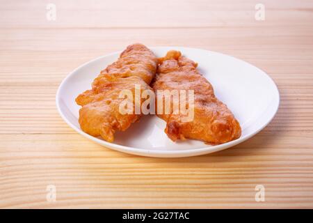 Bananenfritter oder Bananenbraten oder Pazham pori, indischer gebratener Snack, isoliert auf Keramikplatte mit Holzhintergrund. Stockfoto