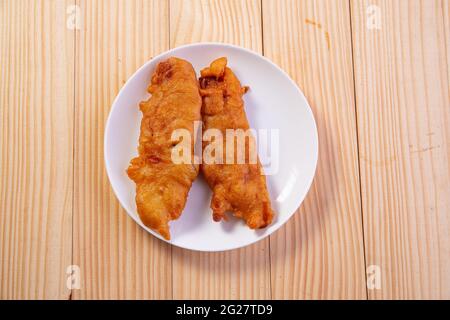 Bananenfritter oder Bananenbraten oder Pazham pori, indischer gebratener Snack, isoliert auf Keramikplatte mit Holzhintergrund. Stockfoto