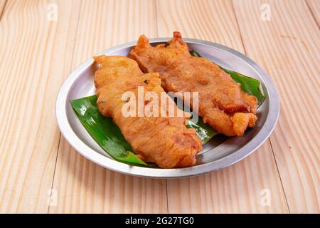 Bananenfritter oder Bananenbraten oder Pazham pori, indischer gebratener Snack, isoliert auf Stahlplatte, mit Bananenblatt auf Holzgrund ausgekleidet. Stockfoto