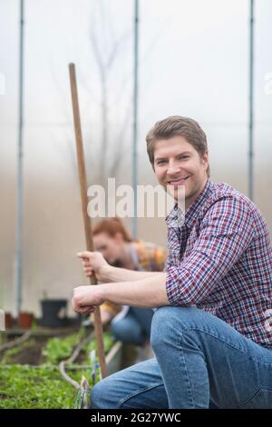 Mann mit Rechen hockte in der Nähe des Gartenbetts Stockfoto