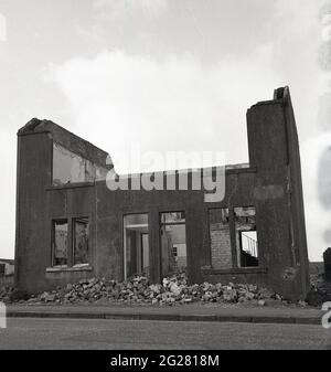 1960er Jahre, historisch, am Straßenrand und Außenansicht eines Paares verlassene alte Reihenhäuser, mit den Dächern und oberen Stockwerken weg und mit Ziegeln, altem Mauerwerk und Schutt liegen auf dem Boden, Kelty, Fife, Schottland, Großbritannien. Als Kohlebergbaudorf an der Grenze zu Fife und Perthshire stand das Dorf in dieser Zeit vor einer ungewissen Zukunft, da die Kohlebergwerke, die seit 1873, als die erste Tiefmine, die Lindsey Mine, versenkt wurde, einst viele hundert lokale Arbeiter beschäftigt hatten, geschlossen oder aufgegeben wurden. Stockfoto