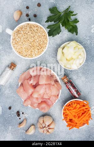 Rohzutaten zum Kochen von Pilaf, braunem Reis und Hühnerfilet, geriebenen Karotten und gehackten Zwiebeln, Pfeffer, Tomaten, Knoblauchkräutern und Gewürzen. Grauer Hintergr Stockfoto