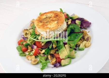 Eine Scheibe Ziegenkäse, serviert auf einem Salatbett, an einem weißen Tisch. Stockfoto