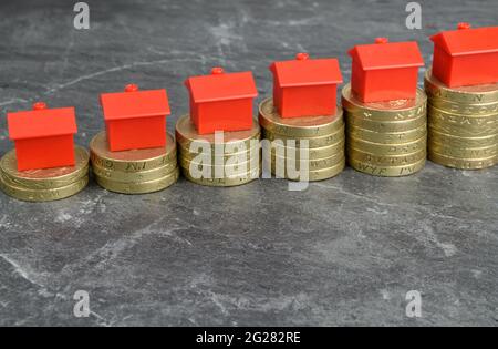 Spielzeughäuser auf steigenden Münzstapeln, mit einem Rechner im Hintergrund. Eine Metapher für Immobilieninvestitionen. Stockfoto