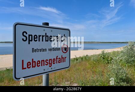 09. Juni 2021, Brandenburg, Großräschen: Am neuen Stadtstrand am Großräschener See steht ein Schild mit der Aufschrift „Sperrbereich - Betreten verboten - Lebensgefahr“. Der neu geschaffene Strand verleiht ein wenig karibisches Flair, wenn man ihn betrachtet. Nach Angaben der Lausitzer und Mitteldeutschen Bergbau-Verwaltungsgesellschaft mbH (LMBV) sind Strand und See weiterhin geschlossen. Der Wasserstand im Großräschensee, ehemals Tagebau Meuro, hat seinen endgültigen Wasserstand noch nicht erreicht. Wo einst der Braunkohlenbergbau die Landschaft dominierte, war New Water para Stockfoto