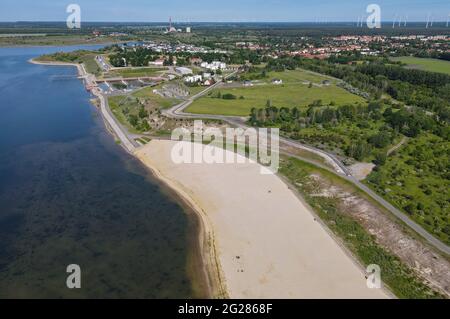 09. Juni 2021, Brandenburg, Großräschen: Der helle Sand des Stadtstrandes am Großräschener See scheint in der Morgensonne (Luftaufnahme mit Drohne). Der neu geschaffene Strand verleiht ein wenig karibisches Flair, wenn man ihn betrachtet. Nach Angaben der Lausitzer und Mitteldeutschen Bergbau-Verwaltungsgesellschaft mbH (LMBV) sind Strand und See weiterhin geschlossen. Der Wasserstand im Großräschensee, ehemals Tagebau Meuro, hat seinen endgültigen Wasserstand noch nicht erreicht. Wo einst der Braunkohlenbergbau die Landschaft dominierte, gibt es derzeit neue Wasserparadiese mit rund 14,000 Hektar Wasser Stockfoto