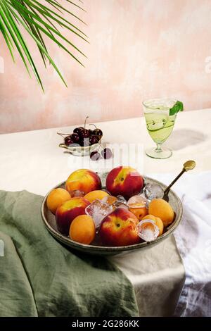 Sommercocktails oder Softdrinks und Obst stehen auf dem Tisch. Rosa Wand und Palmenblätter Hintergrund. Stockfoto