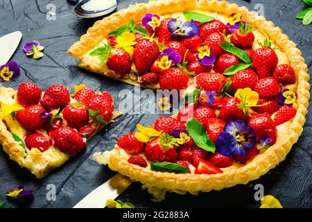 Erdbeerkuchen in Scheiben, verziert mit essbaren Blumen und Minze.Trendy Summer Berry Pie Stockfoto