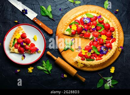 Erdbeerkuchen in Scheiben, verziert mit essbaren Blumen und Minze.Trendy Summer Berry Pie Stockfoto