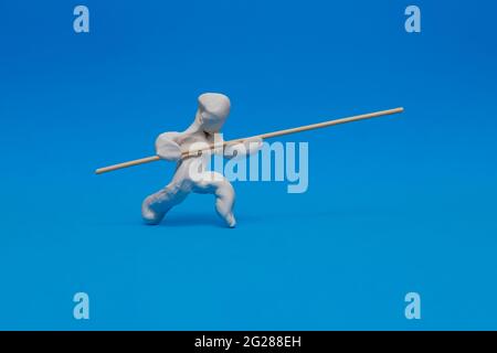 Eine weiße Plastilin-Attrappe, die auf blauem Hintergrund die Pole-Vaulting übt. Der Dummy läuft mit angehobenem Pol und gewinnt an Schwung, um den Sprung zu machen Stockfoto