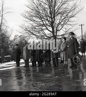 Sechziger Jahre, historischer Tag, der an einem kalten Wintertag draußen steht, beugen eine kleine Gruppe von Männern und eine Frau die Köpfe zu Ehren derer, die in den beiden Weltkriegen kämpften und starben, Kelty, Fife, Schottland, Großbritannien. Stockfoto