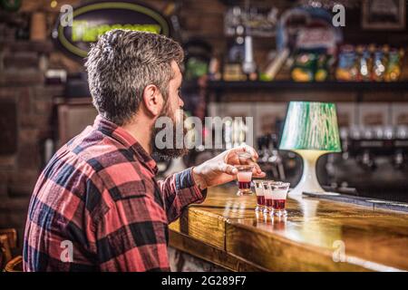 Trinken von Alkohol in Schnapsgläser in einem Nachtclub oder einer Bar. Bärtiger Mann Schüsse Cocktail. Tequila Shots, Wodka, Whisky, Rum. Barkeeper im Pub. Tequila-Schuss Stockfoto