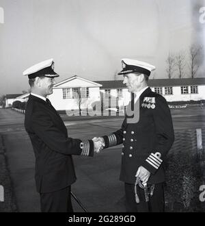 1960er Jahre, historisch, außerhalb der HMS Calendonia, zwei Royal Naval Captains, die sich die Hände schüttelten, in einer Übergabe des Kommandos, Fife, Schottland. Captain (Capt) ist ein hochrangiger Offizier der Royal Navy, über einem Commander und unter Commodore und hat einen NATO-Ranking-Code von OF-5. Der Rang entspricht einem Oberst der britischen Armee und der Royal Marines sowie einem Gruppenkapitän der Royal Air Force. Die HMS Caledonia wurde 1937 eröffnet und war bis 1985 für die Ausbildung von Handwerkern verantwortlich, wobei viele Tausende von jungen Männern eine Ausbildung durchgemacht haben. Stockfoto