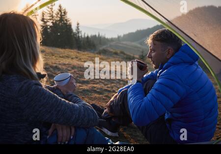 Nahaufnahme aus dem Innenzelt von ein paar Freunden, die im Zelt sitzen und heißen Tee trinken, während sie die wunderschöne Umgebung betrachten. Camping in den Bergen an sonnigen Tagen. Stockfoto