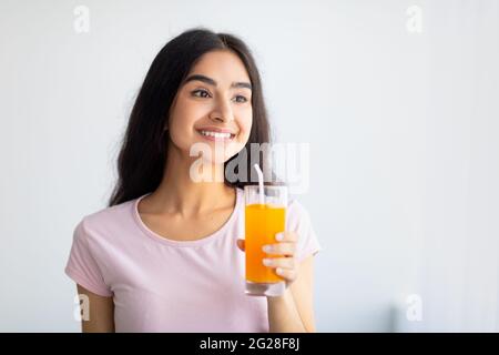 Eine fröhliche indische Frau hält drinnen ein Glas erfrischenden Fruchtsafts. Sommer Detox, Wellness, Diät-Konzept Stockfoto