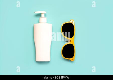 Sommerferienkonzept.Draufsicht auf gelbe Sonnenbrille und eine Flasche Sonnencreme auf blauem Hintergrund