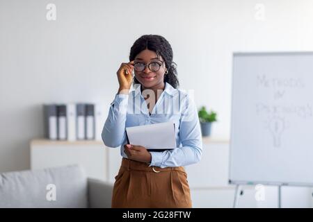 Professionelle Psychotherapie. Porträt einer jungen schwarzen Psychologin, die Clipboard hält und die Kamera im Büro anlächelt Stockfoto