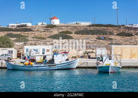 Griechenland. Koufonisi Island, Kykladen, 23. Mai 2021. Traditionelle hölzerne Fischerboote, die am Hafendock festgemacht sind, weiße Gebäude im Dorf und blauer Himmel Stockfoto