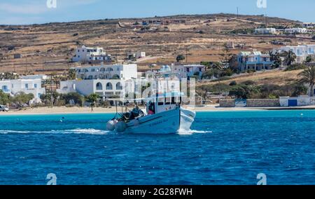 Griechenland. Kykladen, Insel Koufonisi, 23. Mai 2021. Fischerboot auf dem Weg zum Hafen, Sandstrand und traditioneller Dorfhintergrund, sonniger Tag. Sommer Stockfoto