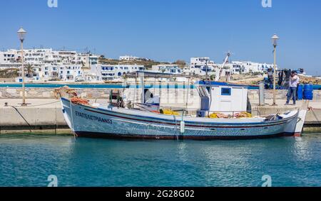 Griechenland. Koufonisi Island, Kykladen, 22. Mai 2021. Traditionelles Fischerboot aus Holz, das am Hafendock festgemacht ist, weiße Gebäude im Dorf und ein blauer Himmel Stockfoto