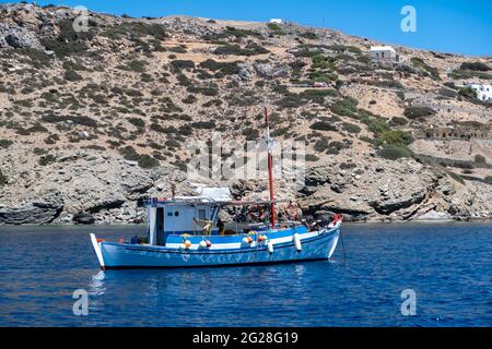 Griechenland, Insel Koufonisi. Kykladen. 23.Mai 2021. Fischerboot verankert auf ruhigen Meer, felsige Landschaft Hintergrund. Fischer, die mit den Netzen arbeiten. Trad Stockfoto