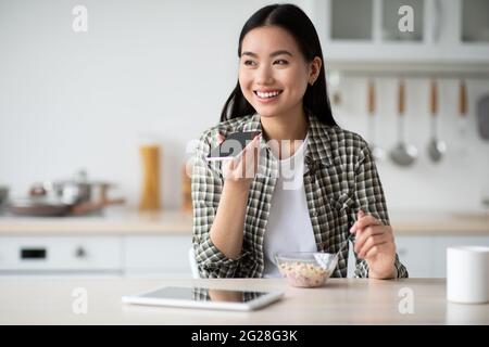 Lächelnde asiatische Frau, die beim Essen Sprachnachrichten aufzeichnet Stockfoto