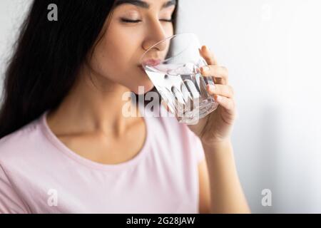 Junge Inderin trinkt zu Hause klares Mineralwasser aus Glas, selektiver Fokus. Gesundes Leben und Entgiftungskonzept Stockfoto