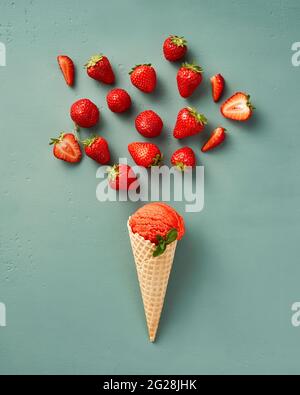 Frisches Erdbeereis im Kegel mit Erdbeeren auf blauem Hintergrund. Italienisches Gelato von oben. Konzept der Eisdiele Stockfoto