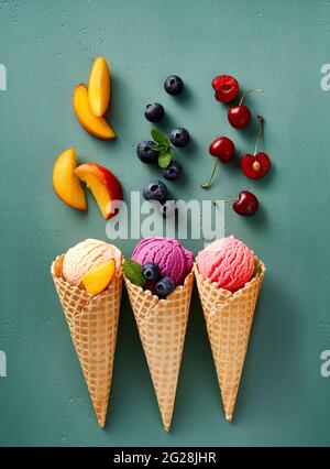 Verschiedene Eiscreme in Zapfen auf blauem Hintergrund. Bunte Eiscreme in verschiedenen Geschmacksrichtungen. Eiscreme mit Nüssen, Früchten und Beeren isoliert. Stockfoto