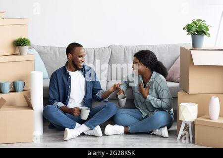 Fröhliches Schwarzes Paar Trinkt Kaffee Zwischen Den Boxen Nach Dem Umzug In Die Neue Wohnung Stockfoto
