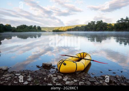 Gelbes Packfloß Gummiboot mit roter Pfanne auf einem Sunrise River. Packrafting. Aktives Lebenskonzept Stockfoto