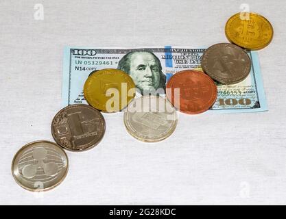 Verschiedene Kryptowährungsmünzen auf einem 100-Dollar-Schein, die wie der Markt nach oben und unten gehen. Stockfoto