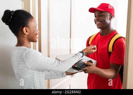 Afrikanische Frau, Die Zu Hause Für Pizza Mit Smartwatch Courier Zahlte Stockfoto