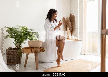 Afrikanische Frau Holding Feuchtigkeitscreme Tun Hautpflege Routine Im Badezimmer Stockfoto