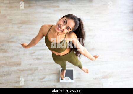 Über Ansicht der tausendjährigen indischen Dame tanzen auf einer Waage, die Wahl eines gesunden Lebensstils, glücklich mit Schlankheitsergebnis Stockfoto